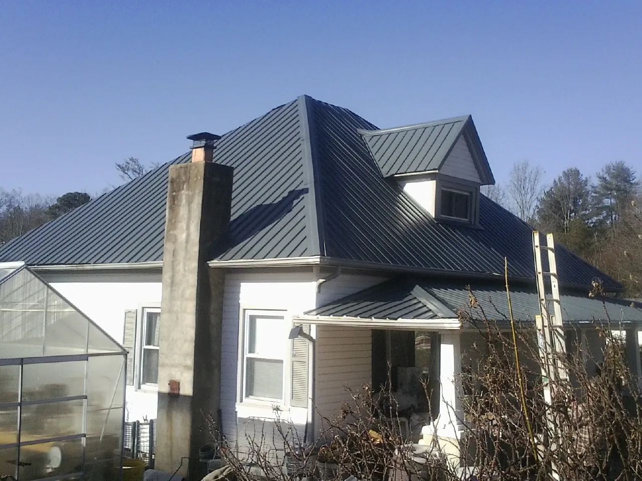 Dark blue standing seam metal roof on a white farmhouse with dormer — Slate & Tile Roof Repair by Roofing Brothers in Atomic City