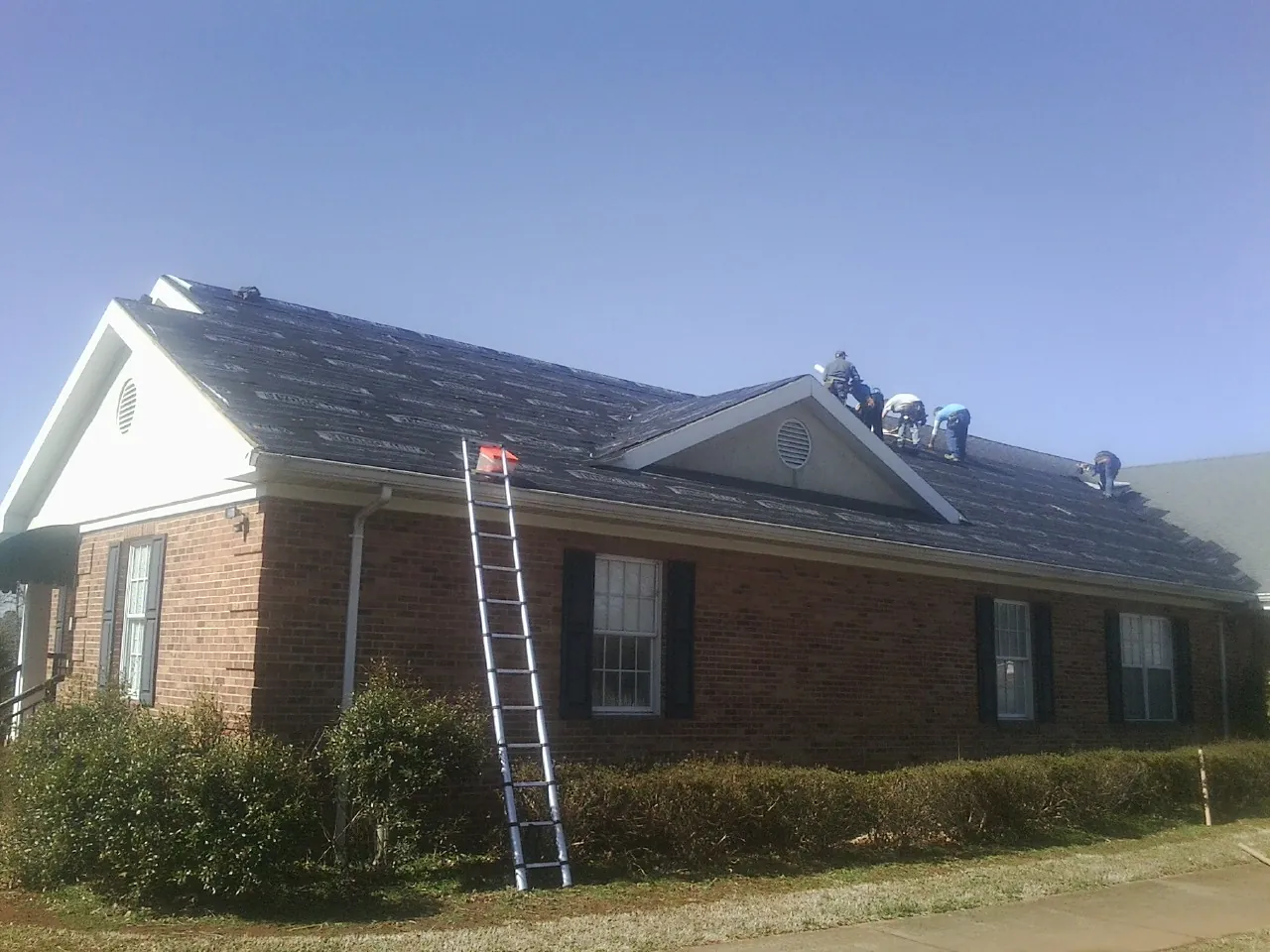 Crew tearing shingles off a brick ranch roof with a ladder set — Metal Roof Repair work by our crew in Atomic City
