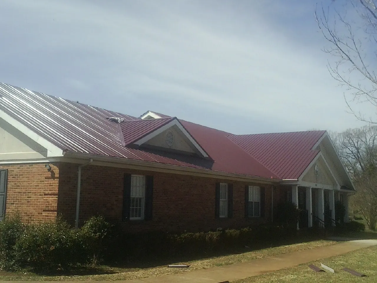Red metal roof with gabled entries on a long brick building, from a Hail Damage Roof Repair job in Atomic City