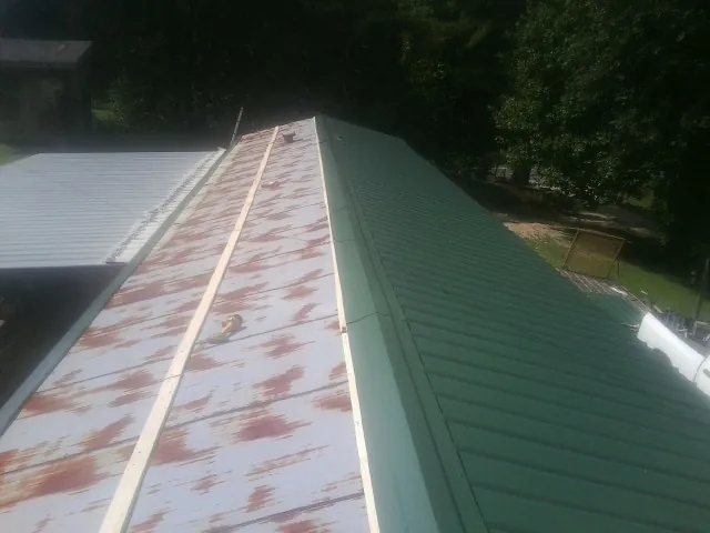 Old rusted panels beside newly installed green metal roofing — Wind Damage Roof Repair by Roofing Brothers in Atomic City