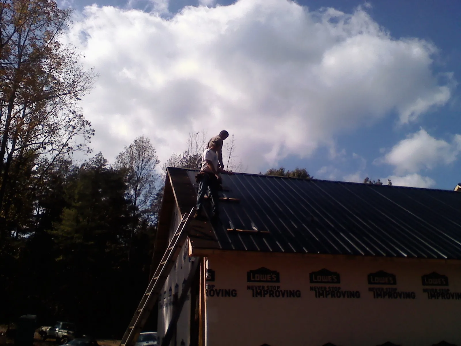 Roofer fastening dark metal panels high against a cloudy sky, from a Roof Inspection job in Atomic City