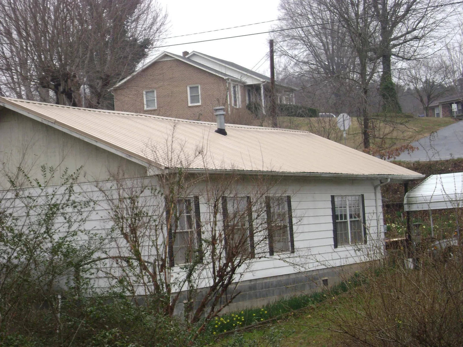 Tan metal roof on a white sided house set into a hillside — Commercial Roofing by Roofing Brothers in Atomic City